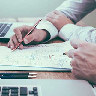 Photo of two
people working together at a desk representative of MSI working with the client to plan security.